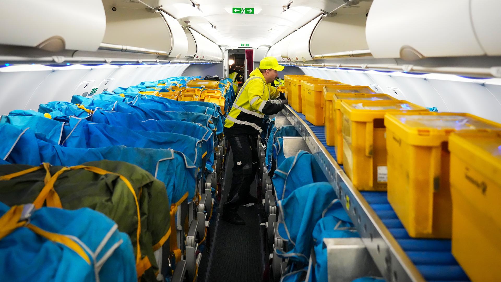 Ein Mitarbeiter schiebt in einem Airbus A320-214 auf dem Flughafen Berlin Brandenburg gelbe Plastikboxen voller Briefe und anderer Post in den vorderen Teil der Kabine.