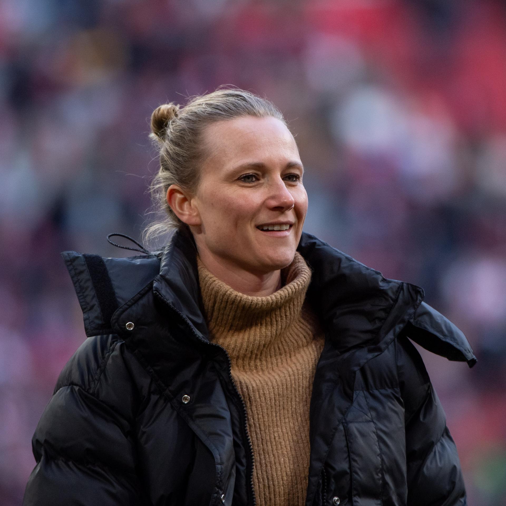 Kathleen Krüger steht am Spielfeldrand, hinter ihr die Tribüne mit FC Bayern-Fans