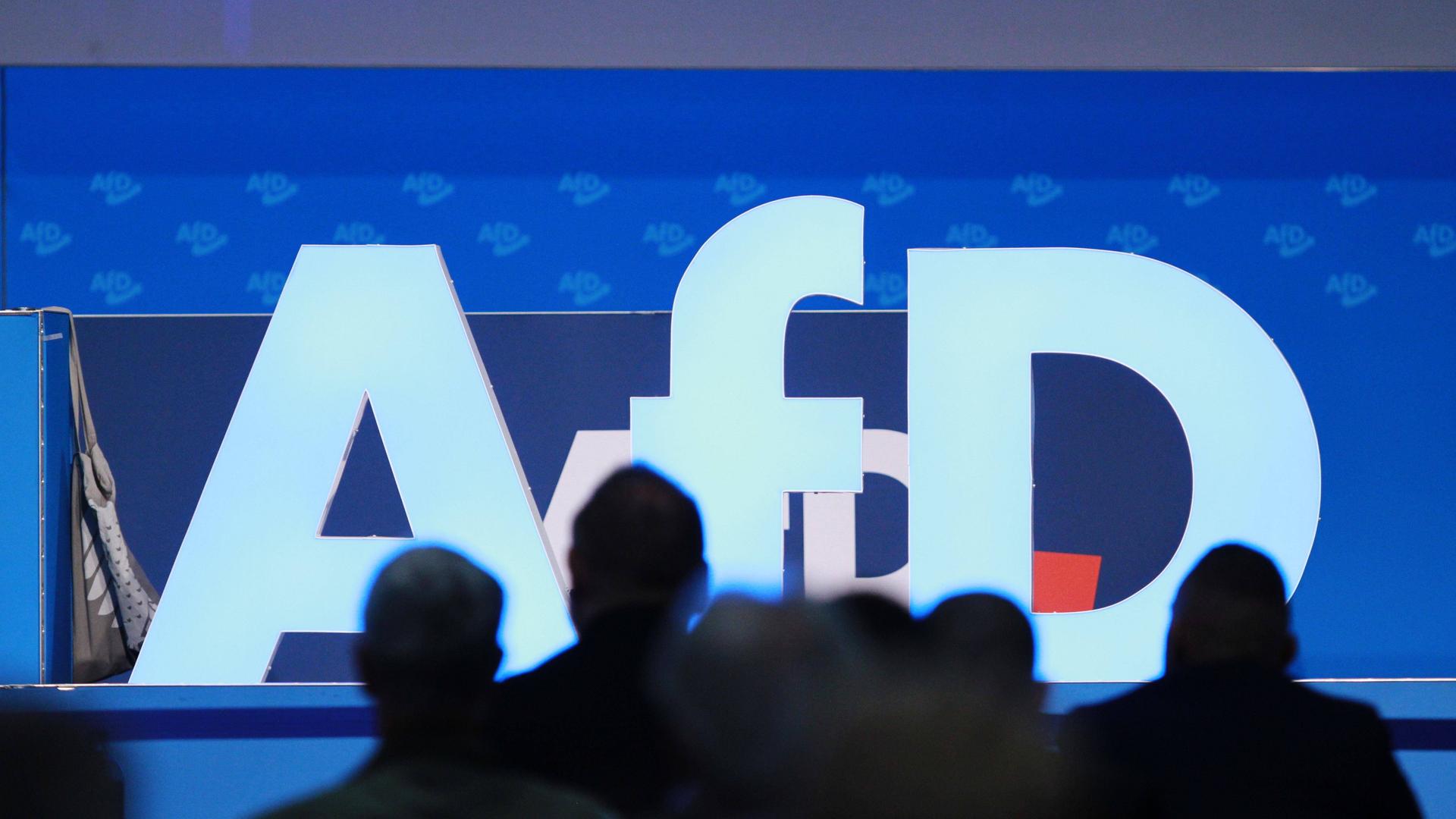 Delegierte sind als Schatten vor dem Logo der AfD auf der Europawahlversammlung in Magdeburg zu sehen.