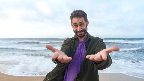 Ein Mann steht am Strand und führt lächelnd ein Selbstgespräch.