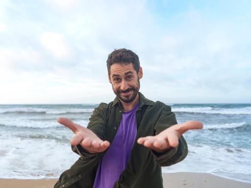 Ein Mann steht am Strand und führt lächelnd ein Selbstgespräch.