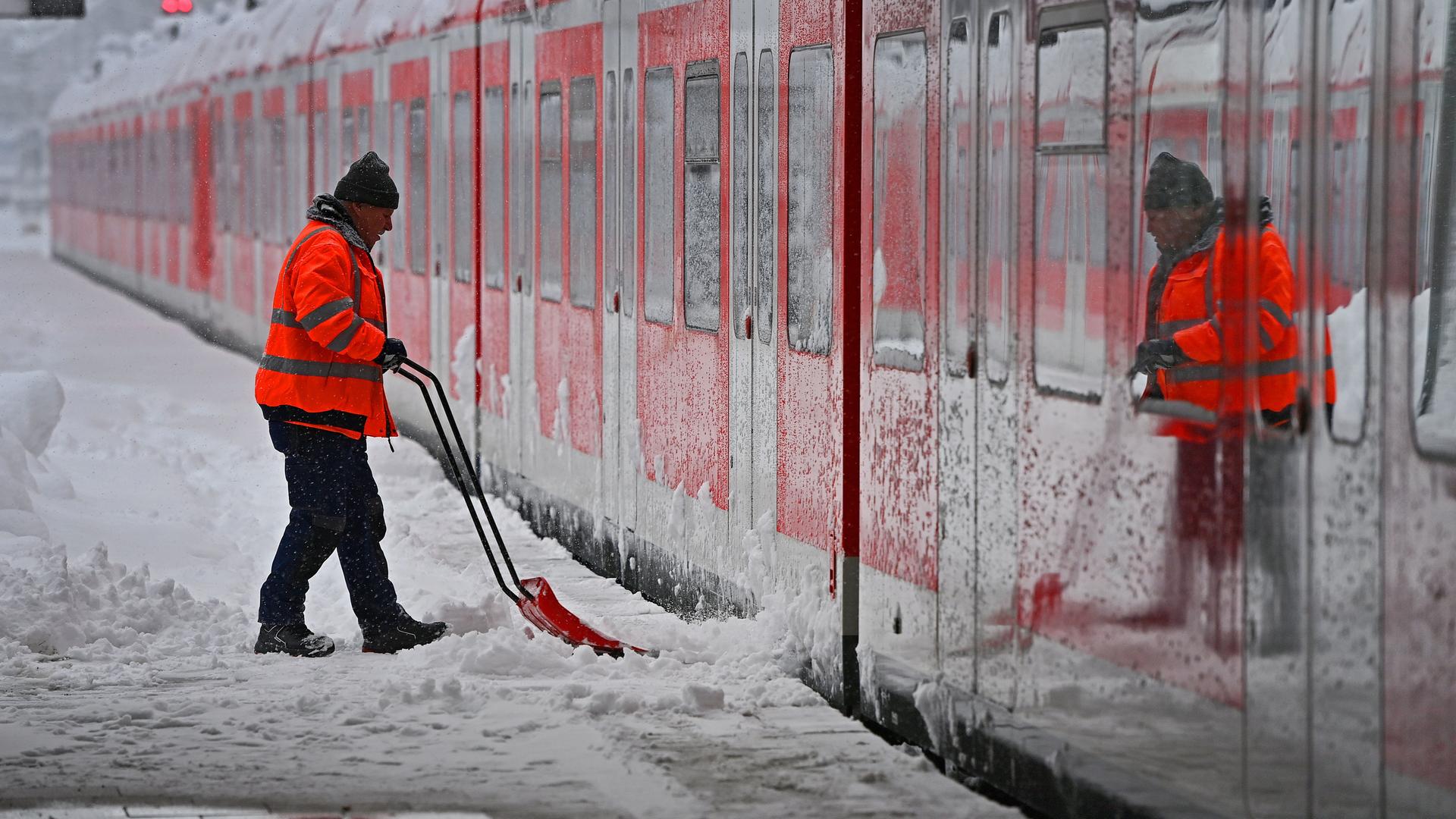 Ein Arbeiter räumt vor einer S-Bahn in München auf einem Bahnsteig den Schnee.