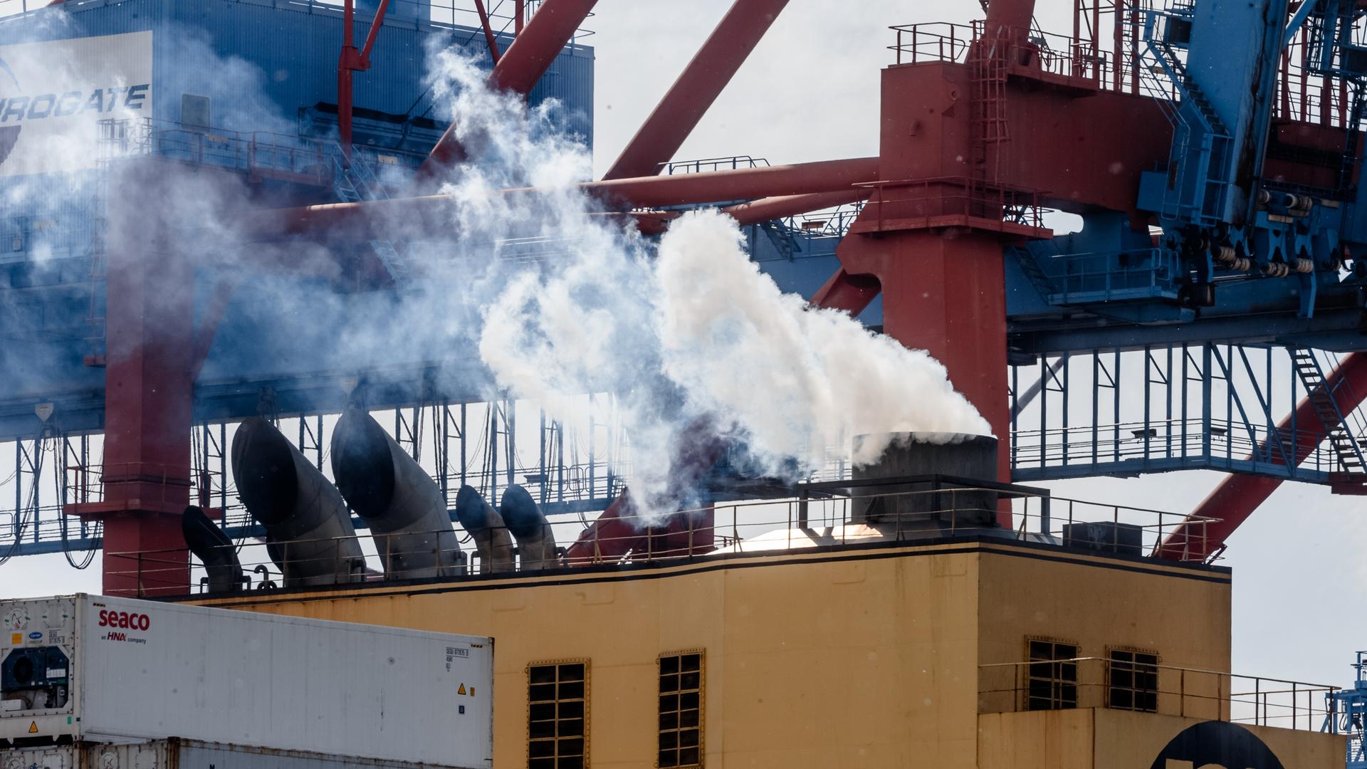 Abgase kommen aus dem Schornstein eines Containerschiffs, während es im Hamburger Hafen am Kai liegt und beladen wird.