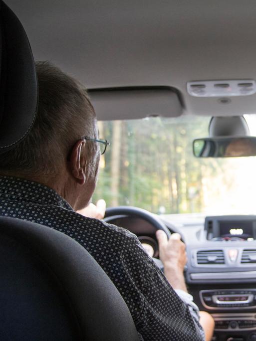 Ein Rentner-Ehepaar sitzt im Auto. Der Mann fährt, die Frau schaut zu ihm herüber.
