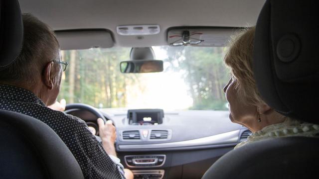 Ein Rentner-Ehepaar sitzt im Auto. Der Mann fährt, die Frau schaut zu ihm herüber.