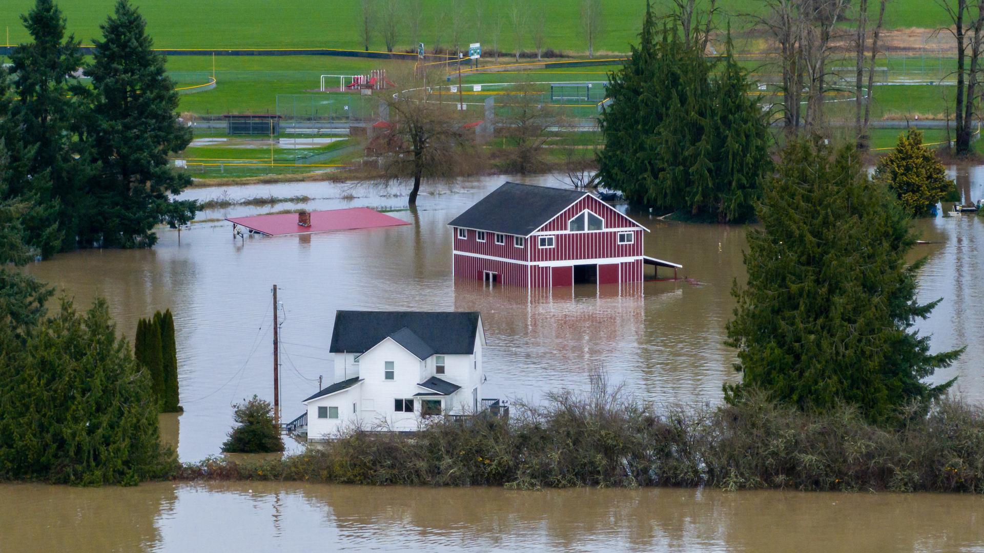 Das Foto ist die Luftaufnahme eines Hauses und einer Scheune, die von Überschwemmungen umgeben sind. Das Foto ist die Luftaufnahme eines Hauses und einer Scheune, die von Überschwemmungen umgeben sind.