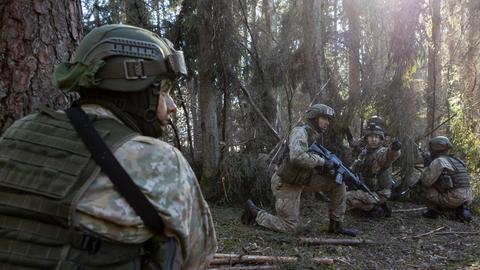 Bewaffnete Soldaten knien bei einem militärischen Übung in einem Waldstück, um Deckung zu nehmen.