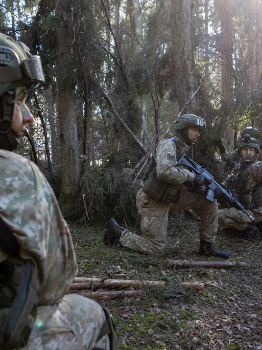 Bewaffnete Soldaten knien bei einem militärischen Übung in einem Waldstück, um Deckung zu nehmen.