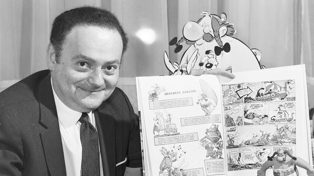 Schwarzweiß-Aufnahme von René Goscinny, der stolz einen Band seiner "Asterix"-Reihe präsentiert Schwarzweiß-Aufnahme von René Goscinny, der stolz einen Band seiner "Asterix"-Reihe präsentiert