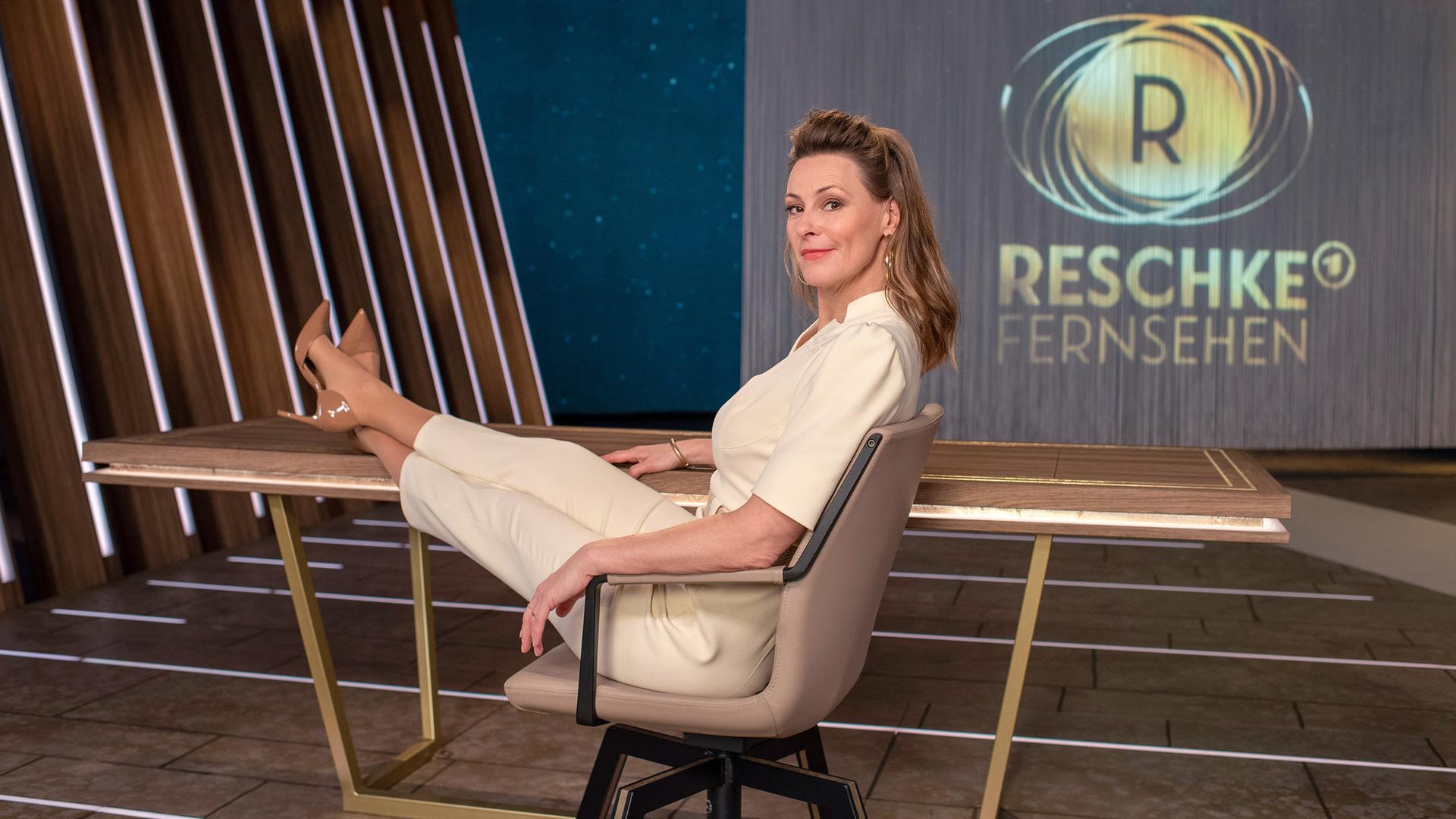 Anja Reschke sitzt in einem Bürostuhl mit den Füßen auf dem Tisch. Im Hintergrund zeigt ein Screen das Sendelogo für "Reschke Fernsehen".