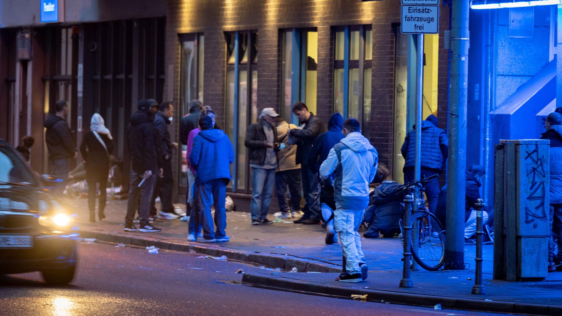 Menschen stehen abends im Frankfurter Bahnhofsviertel vor einem Drogenkonsumraum.