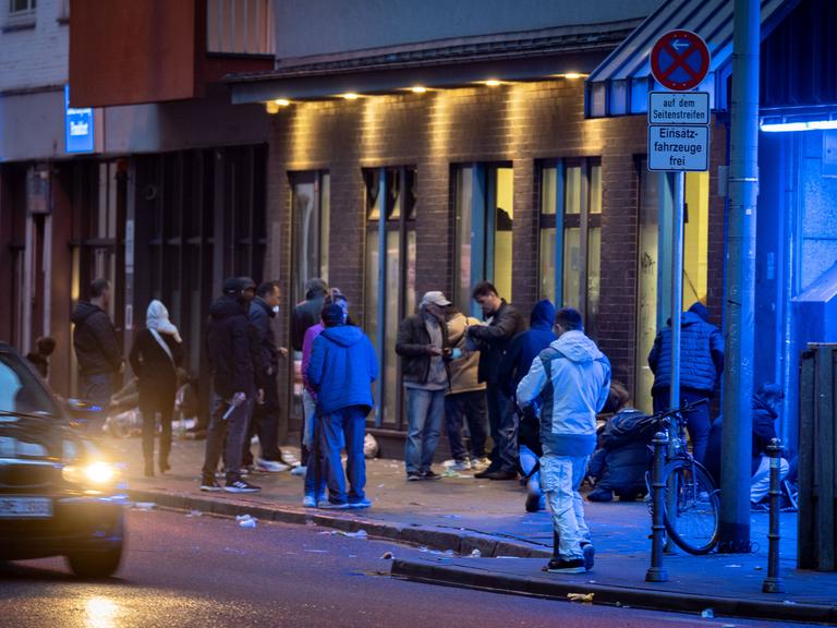 Menschen stehen abends im Frankfurter Bahnhofsviertel vor einem Drogenkonsumraum.