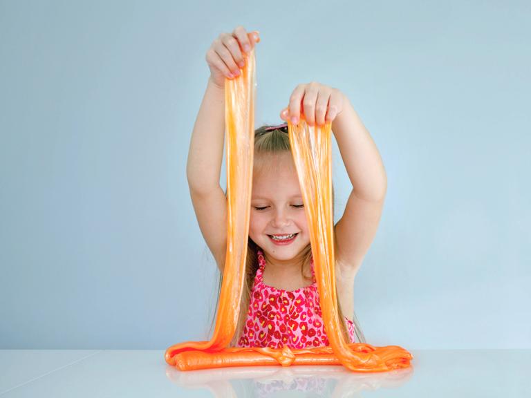Ein Mädchen spielt mit einer großen Portion orangefarbenem Schleim