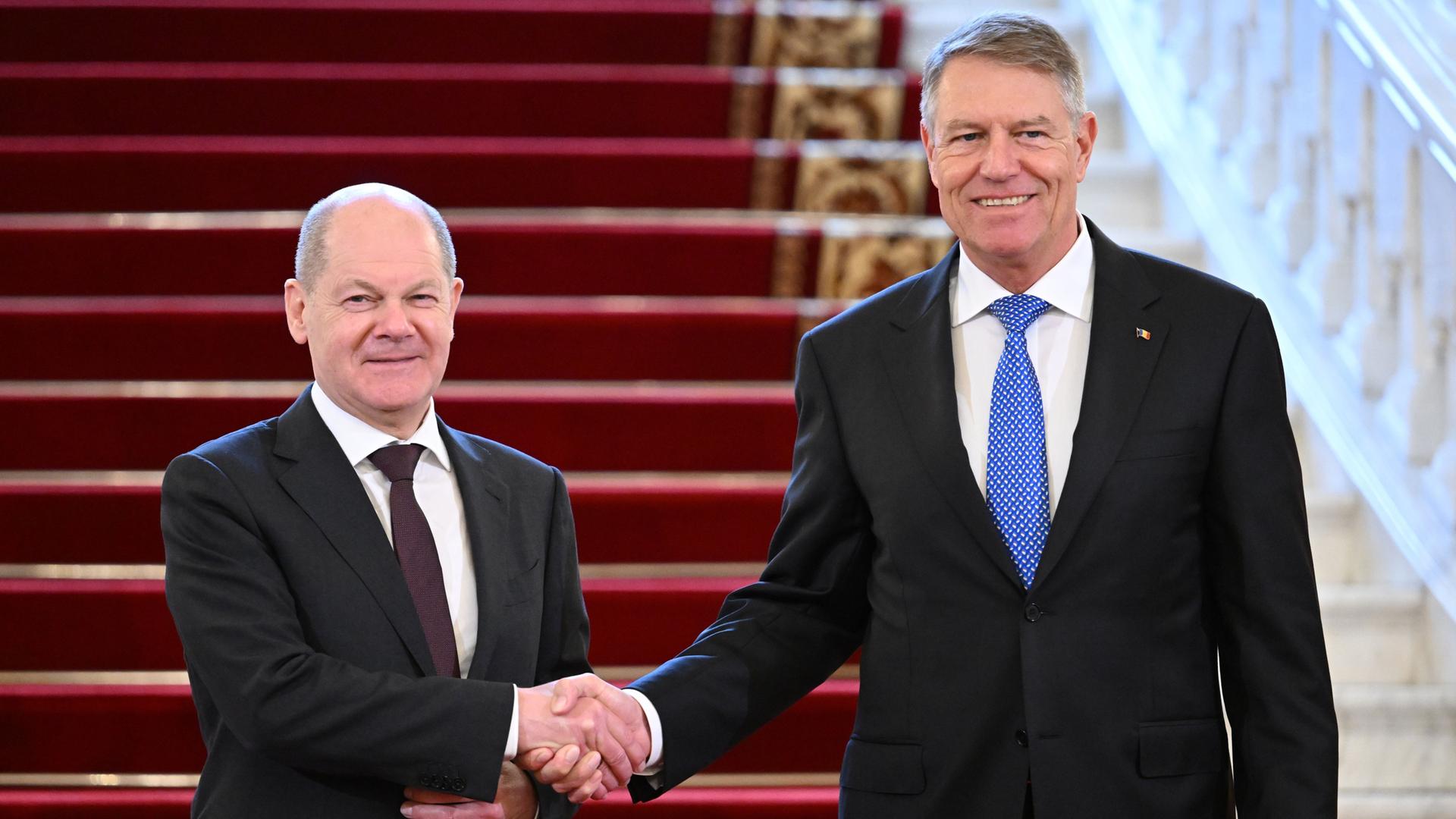 Rumänien, Bukarest: Bundeskanzler Olaf Scholz (SPD, l) und Klaus Iohannis, Präsident von Rumänien, begrüssen sich während des Antrittsbesuchs des deutschen Politikers in der Ehrenhalle des Cotroceni-Palastes.