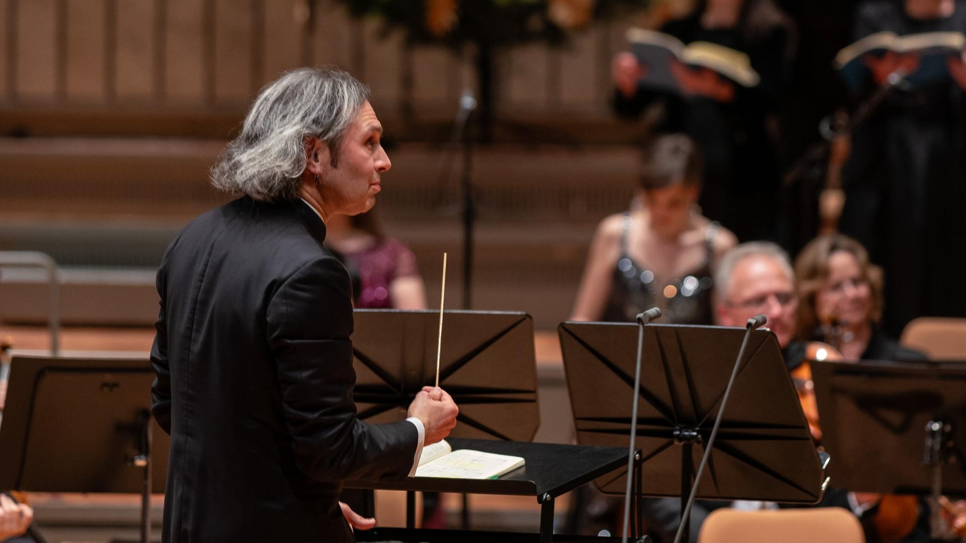 Vladimir Jurowski dirigiert Musiker und Sängerinnen, während auf der Bühne der Philharmonie Berlin ein Weihnachtsbaum steht.