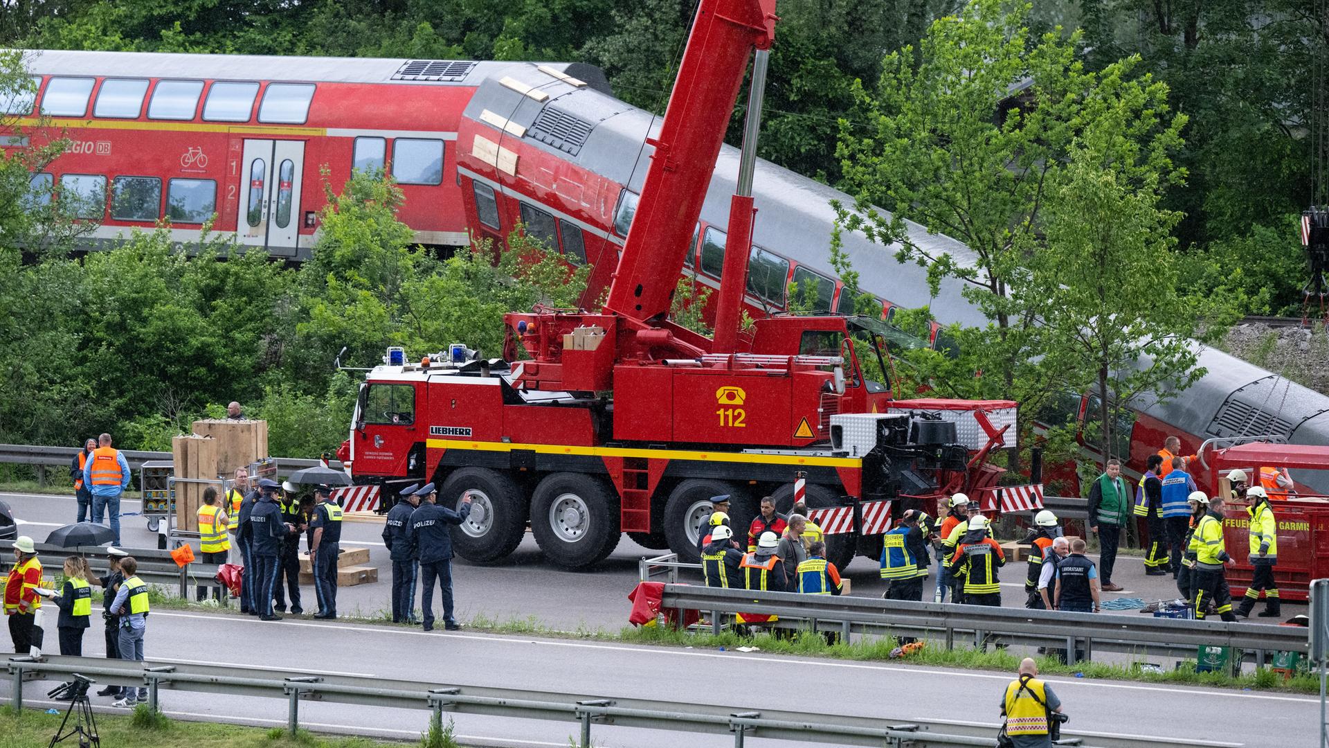 Nach dem schweren Zugunglück sind in Garmisch-Partenkirchen zahlreiche Einsatz- und Rettungskräfte im Einsatz. Im Hintergrund ist der entgleiste Regionalzug zu sehen.