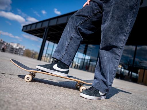 Ein Jugendlicher steht mit einem Bein auf einem Skateboard. 