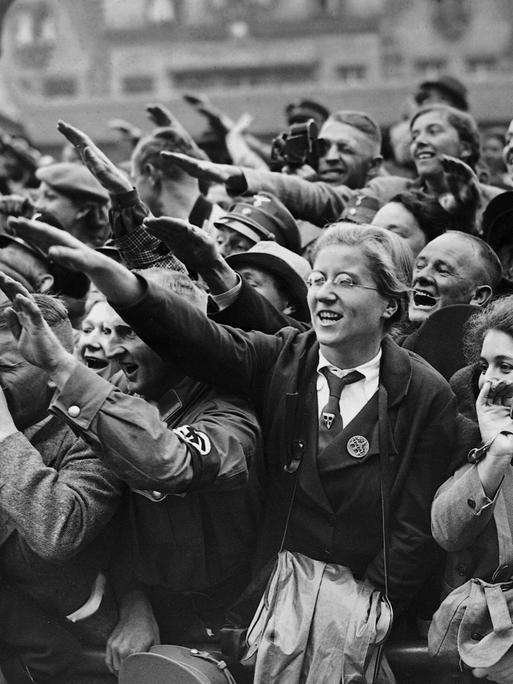 Schwarz-Weiß-Bild von begeisterten Frauen und Männern, die den Hitlergruß zeigen und  dicht gedrängt am Straßenrand stehen