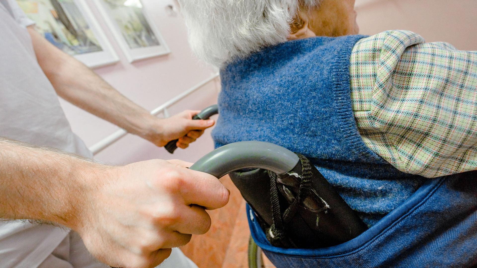 Hände schieben einen Rollstuhl, in der eine ältere Person sitzt. Hände schieben einen Rollstuhl, in der eine ältere Person sitzt.