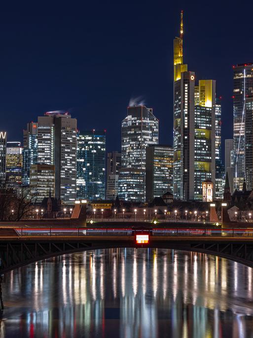 Die Lichter in den Büros der Frankfurter Bankenskyline leuchten am Abend und spiegeln sich im Wasser