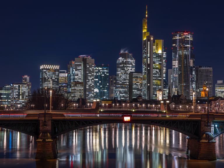 Die Lichter in den Büros der Frankfurter Bankenskyline leuchten am Abend und spiegeln sich im Wasser