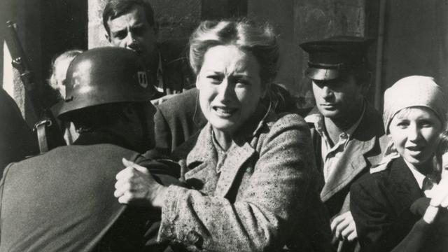 Standfoto aus der Serie "Holocaust", auf dem Meryl Streep von einem Soldaten mit Stahlhelm festgehalten, während sie versucht, sich mit schmerz verzerrtem Gesicht loszureißen.