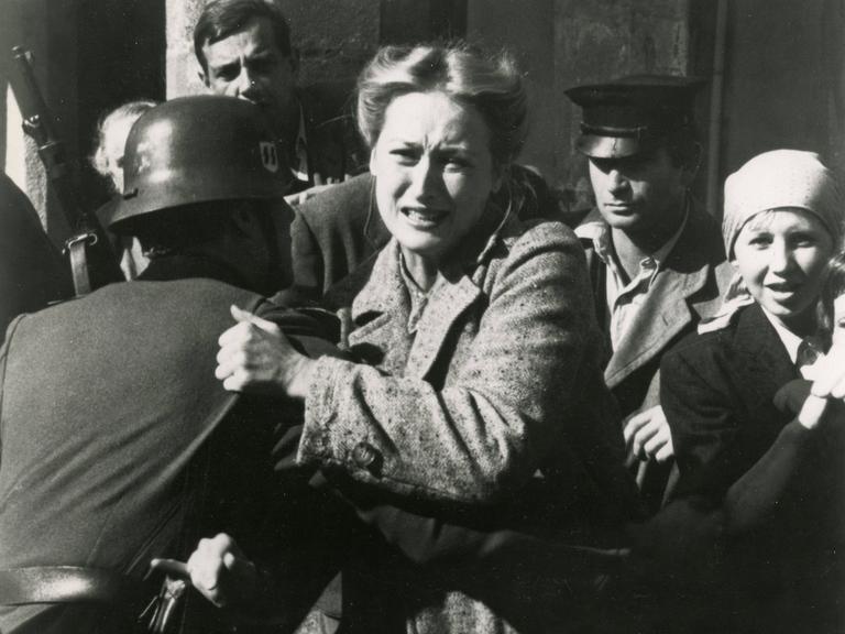 Standfoto aus der Serie "Holocaust", auf dem Meryl Streep von einem Soldaten mit Stahlhelm festgehalten, während sie versucht, sich mit schmerz verzerrtem Gesicht loszureißen. Standfoto aus der Serie "Holocaust", auf dem Meryl Streep von einem Soldaten mit Stahlhelm festgehalten, während sie versucht, sich mit schmerz verzerrtem Gesicht loszureißen.