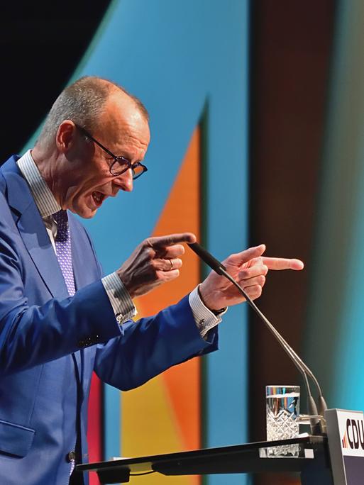 Der CDU-Fraktionsvorsitzende Friedrich merz steht auf einer Bühne und spricht mit erhobenen Armen und ausgestreckten Zeigefingern.