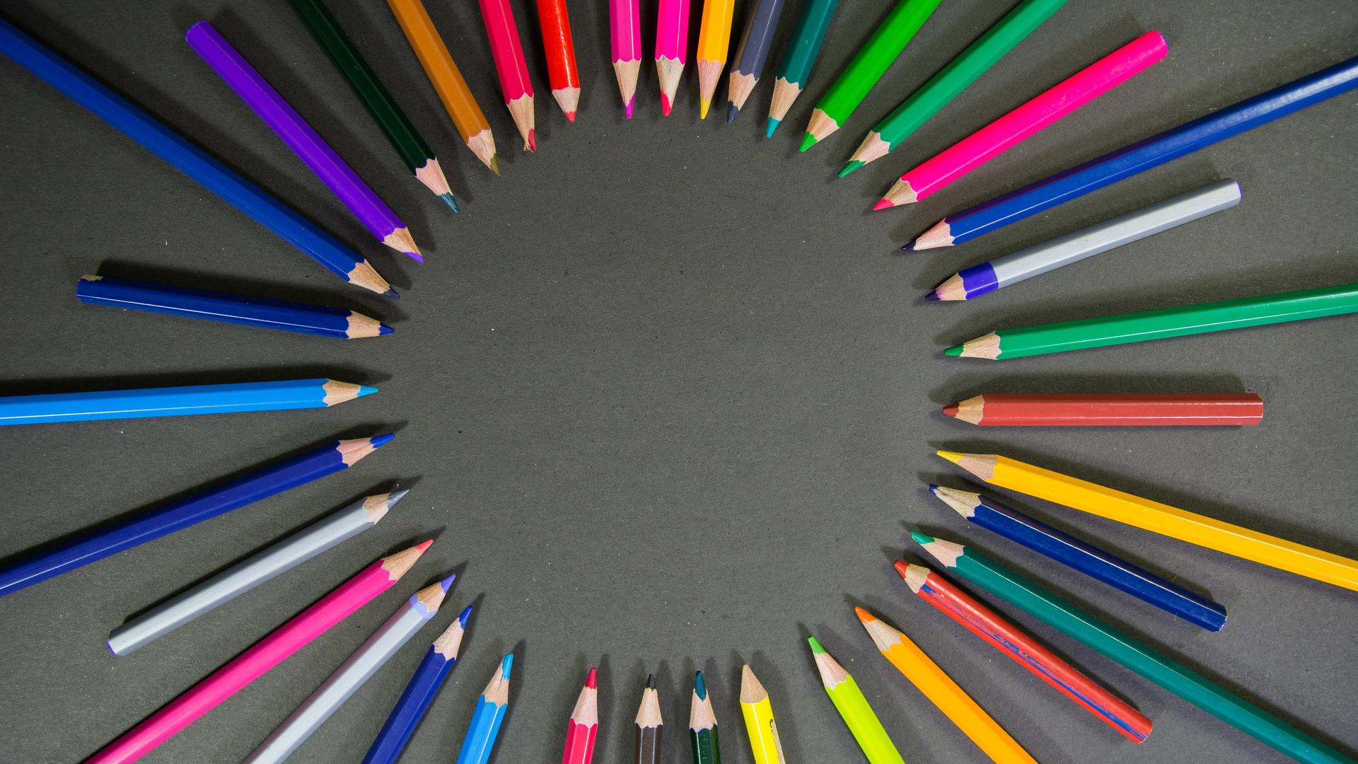 Viele bunte Stifte liegen auf einem grauen Hintergrund aufgefächert