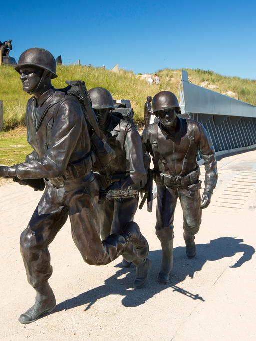 Ein Denkmal zeigt bewaffnete amerikanische Soldaten und ein Landungsboot am Strand in der Normandie. 