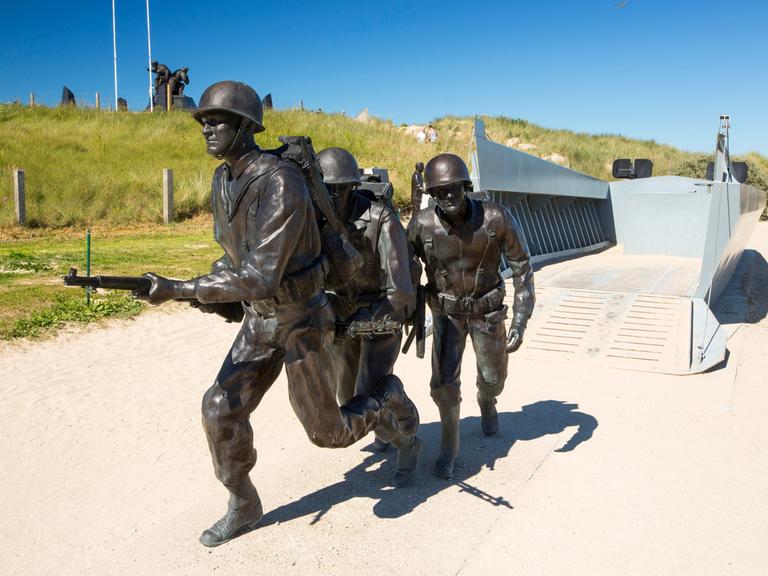 Ein Denkmal zeigt bewaffnete amerikanische Soldaten und ein Landungsboot am Strand in der Normandie. 