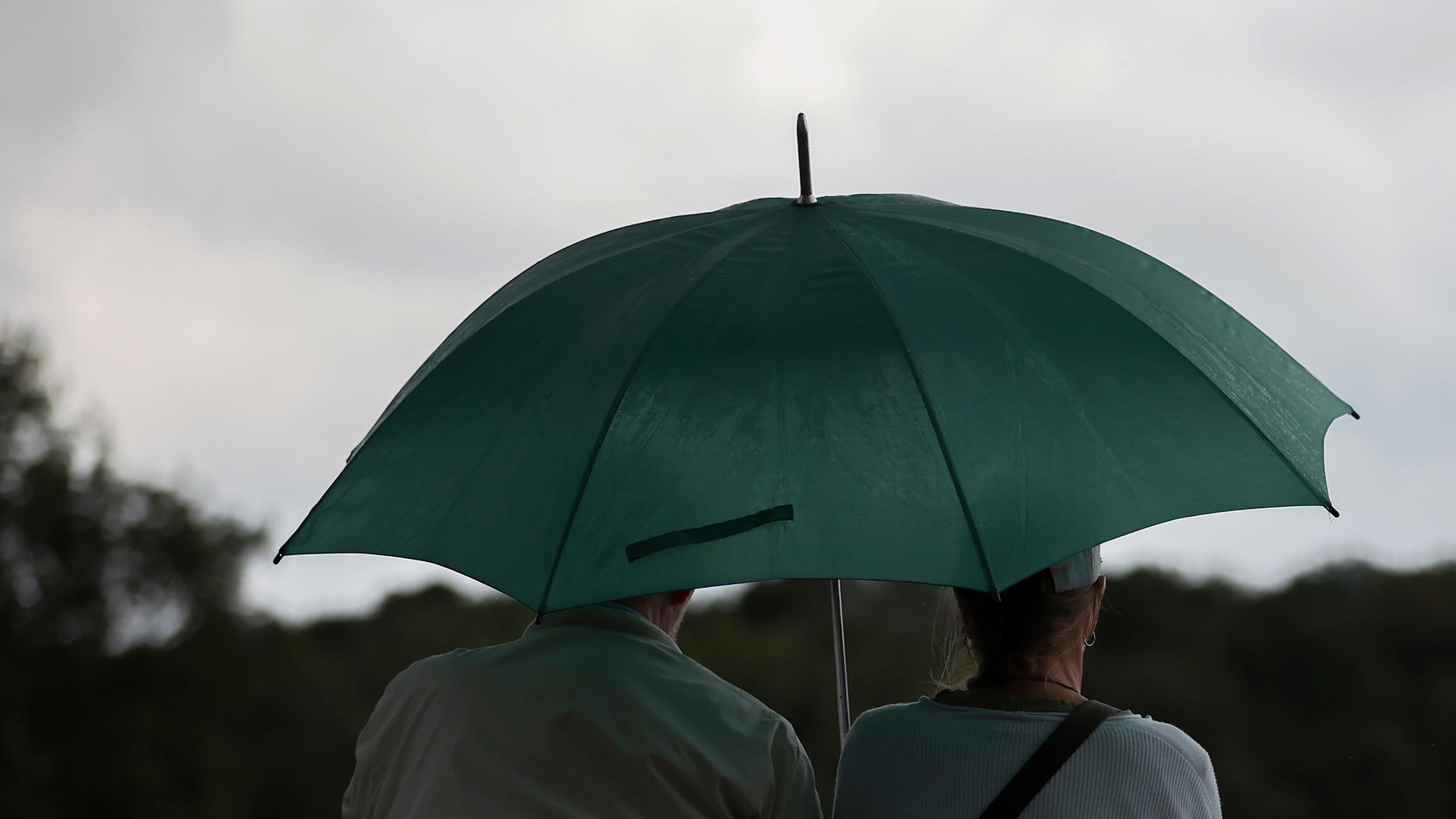 09.08.2024, Hannover, Ein älteres Paar sitzt bei Regen mit grünem Regenschirm auf einer Bank