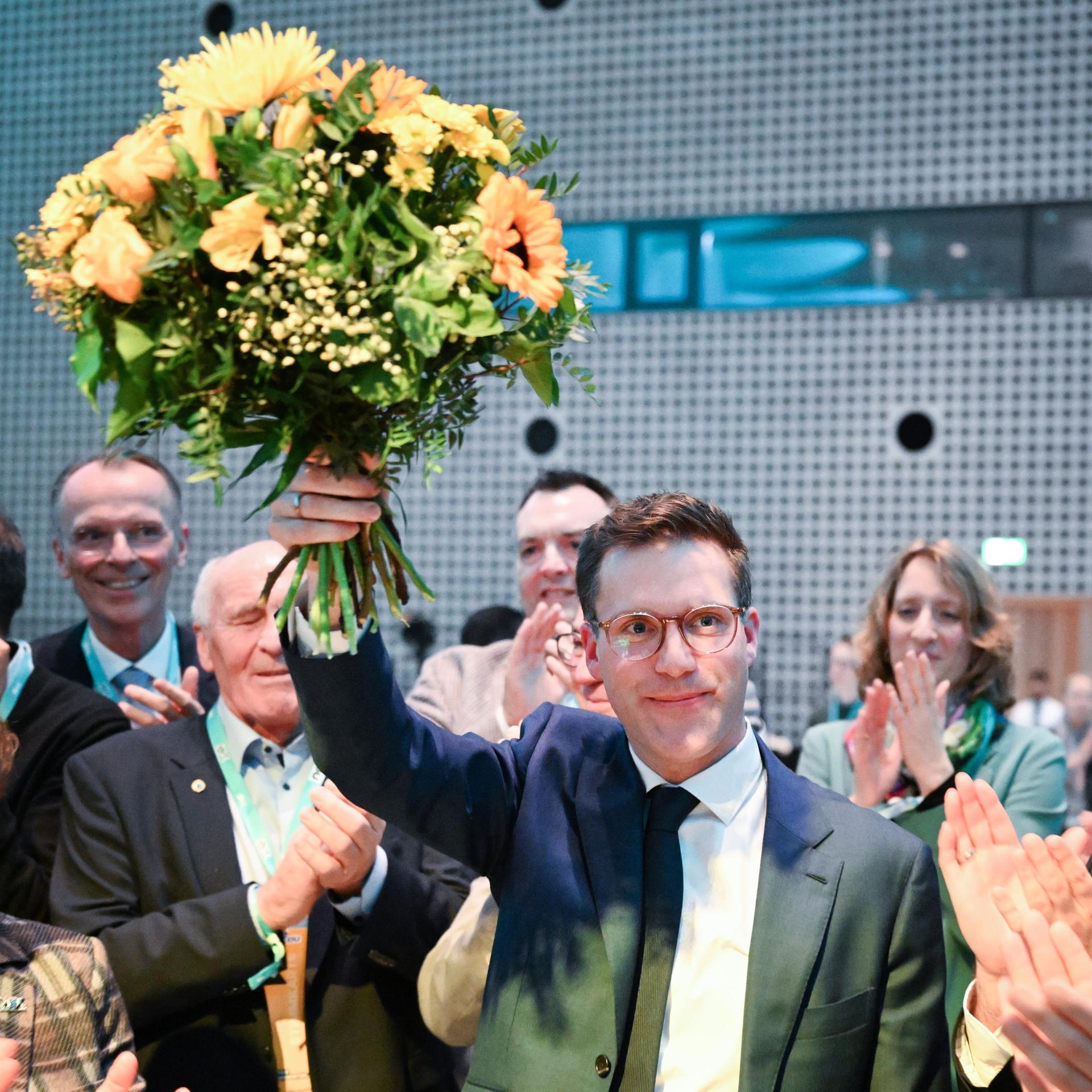 Das Bild zeigt den CDU-Landesvorsitzenden Manuel Hagel auf dem Landesparteitag in Baden-Württemberg. Er hält einen Blumenstrauß in die Höhe, während seine Partei-Kolleginnen und -kollegen ihm zujubeln und Beifall klatschen.