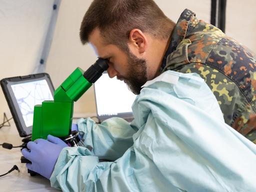 Ein Soldat blickt in einem mobilen Labor an der Sanitätsakademie der Bundeswehr am Institut für Mikrobiologie bei einer Demonstration durch ein Mikroskop. 