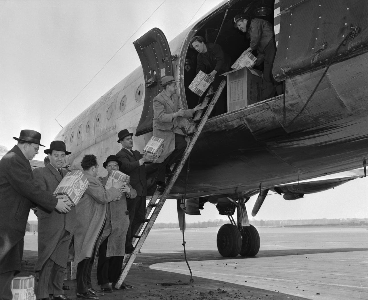 Historisches Schwarz-Weiß-Foto mehrerer Männer, die Pakete aus einem Flugzeug räumen und per Menschenkette weiterreichen.