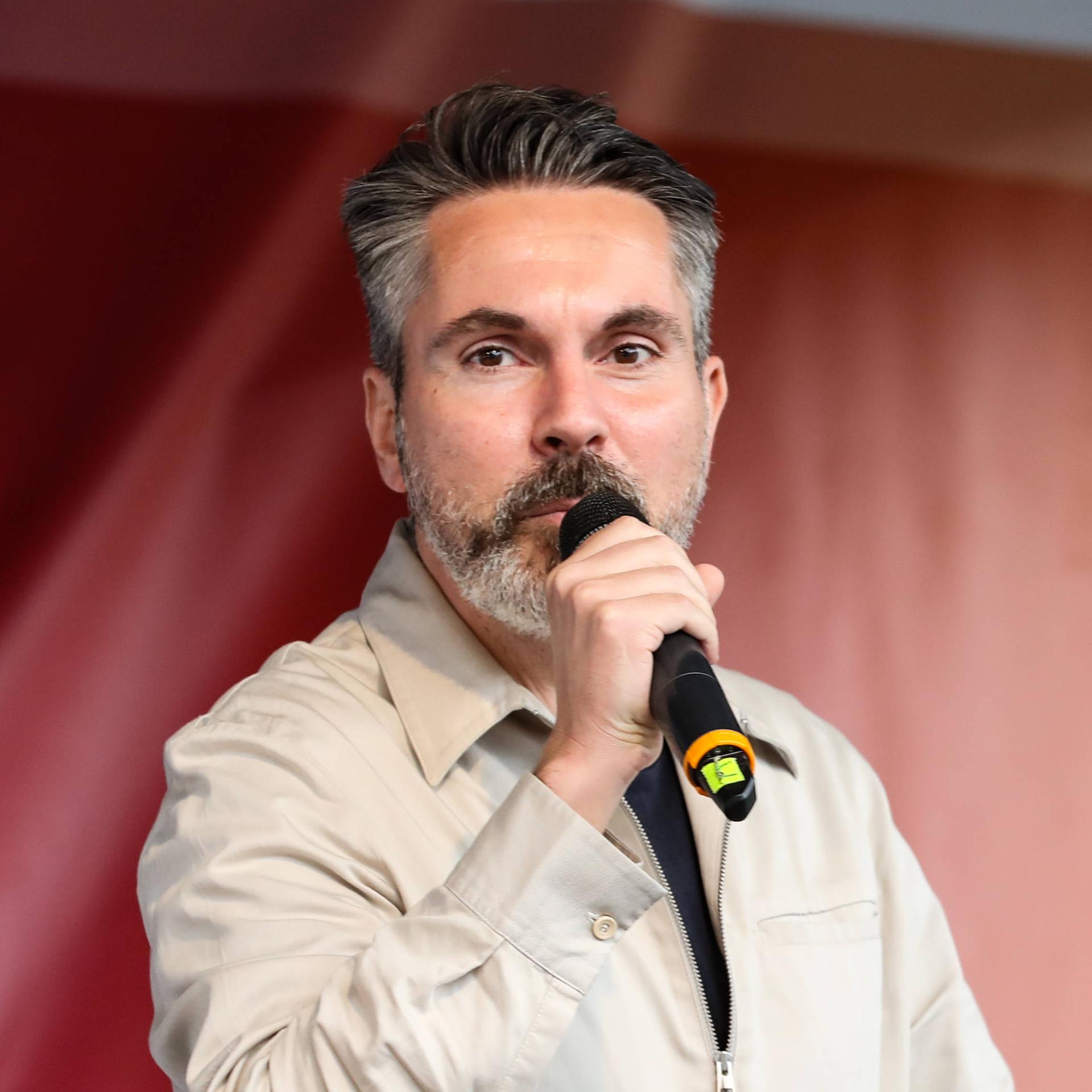 Fabio De Masi spricht in ein Handmikrofon. Im Hintergrund: ein rotes Transparent