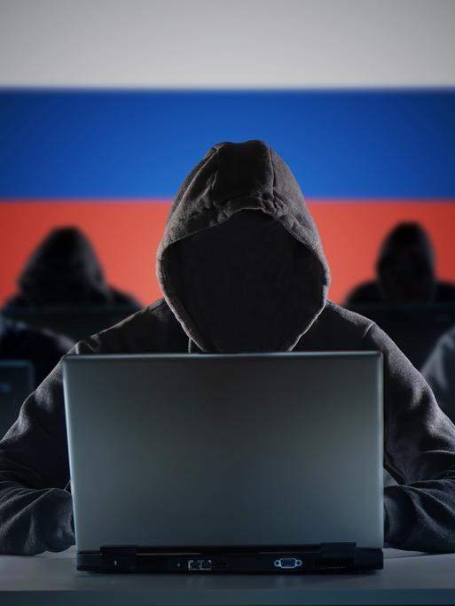 Anonyme russische Hacker vor einem Laptop. Russland Flagge im Hintergrund.