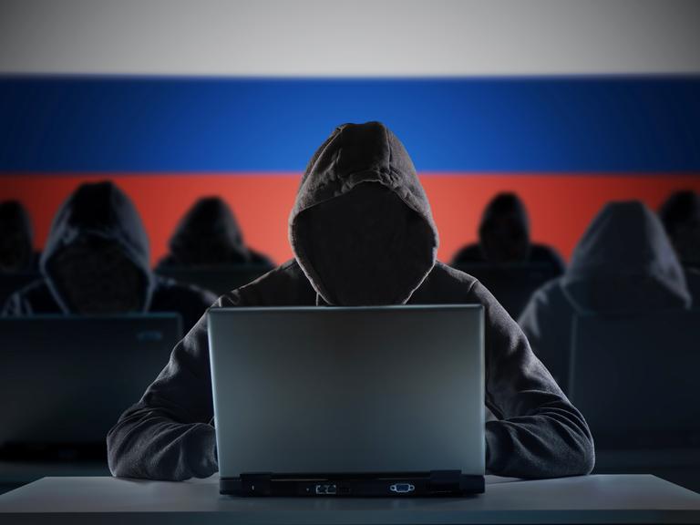 Anonyme russische Hacker vor einem Laptop. Russland Flagge im Hintergrund.