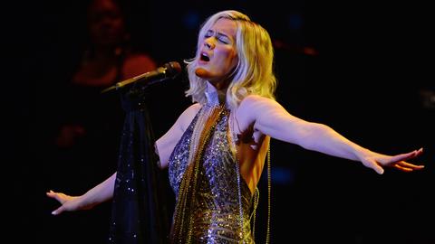 Die Sängerin Joss Stone in einem glitzernden Outfit und ausgebreiteten Armen am Mikrofon.