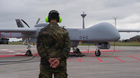Eine Heron-Drohne der Bundeswehr steht auf einem Flugfeld. Davor ein Soldat mit Gehörschutz.