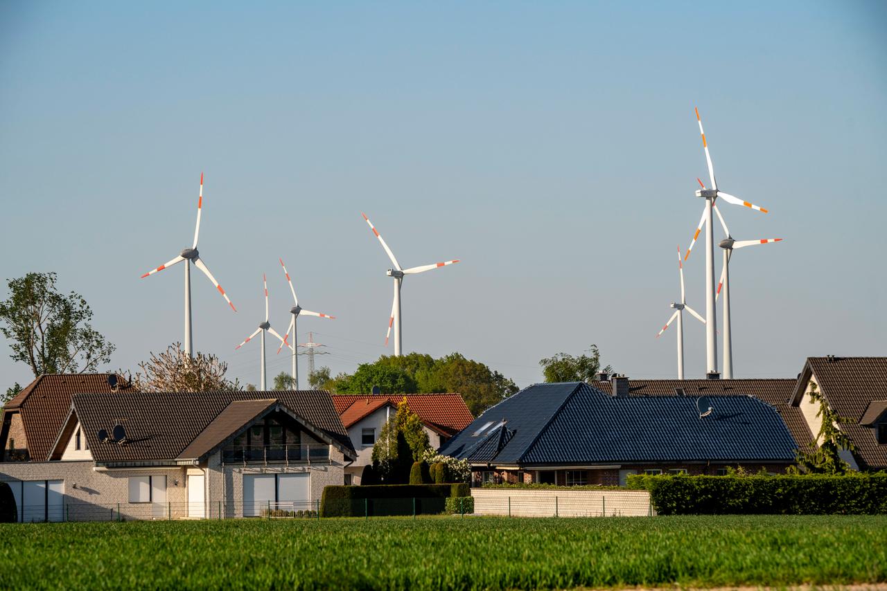 Eine Windkraftanlage steht in der Nähe eines Wohngebiets aus Einfamilienhäusern.