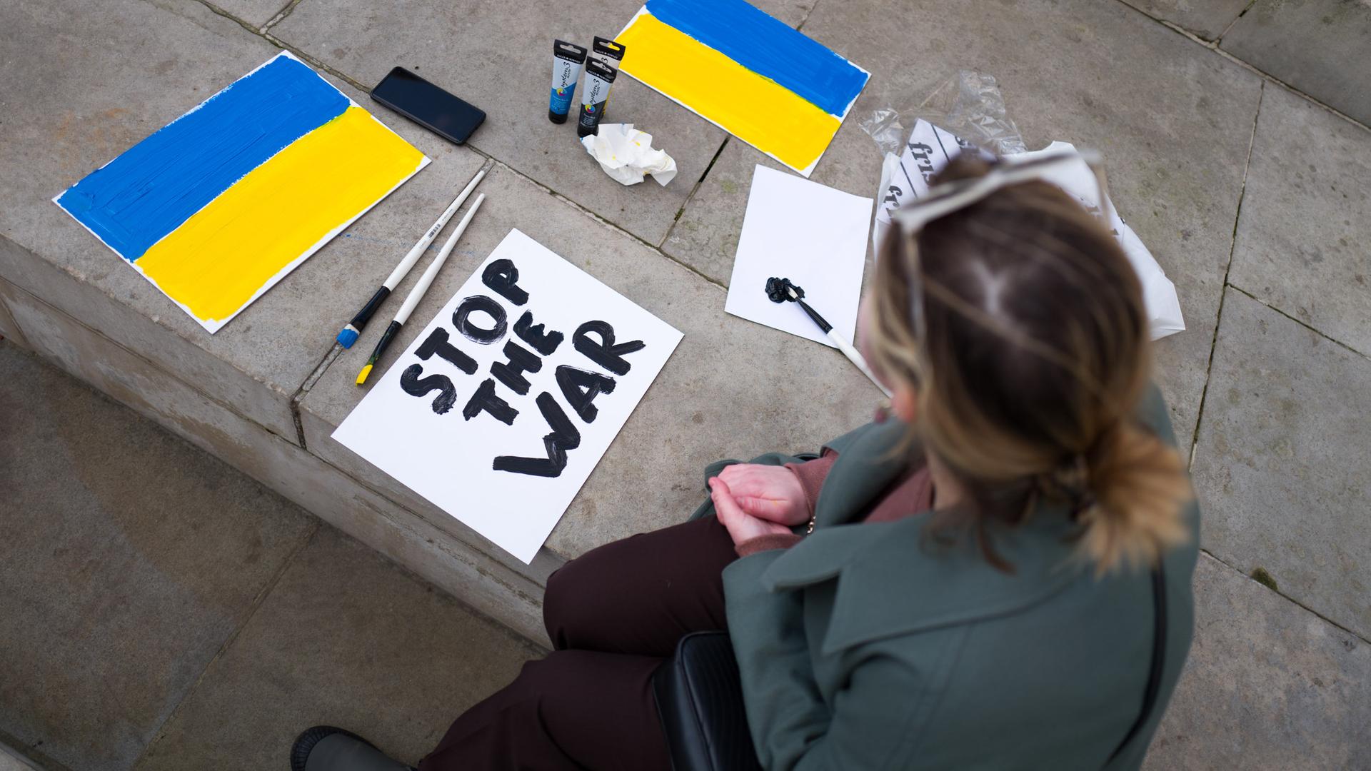 Eine Frau fertigt ein Plakat an mit den Farben der ukrainischen Nationaflagge und den Worten "Stop the war".