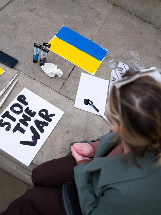Eine Frau fertigt ein Plakat an mit den Farben der ukrainischen Nationaflagge und den Worten "Stop the war".