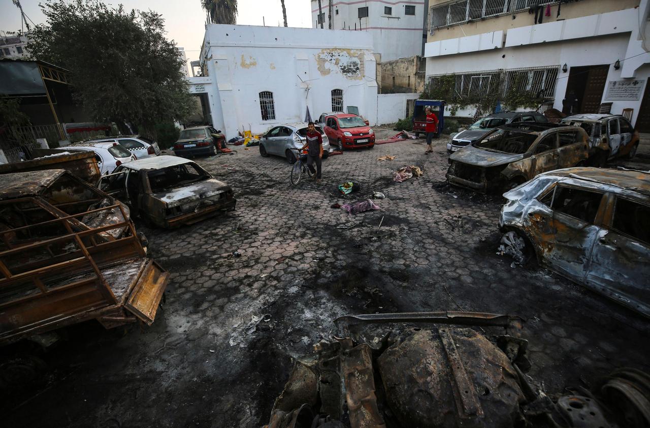 Palästinenser untersuchen einen Parkplatz außerhalb des Krankenhauses in Gaza-Stadt. Man sieht zerstörte Autos.