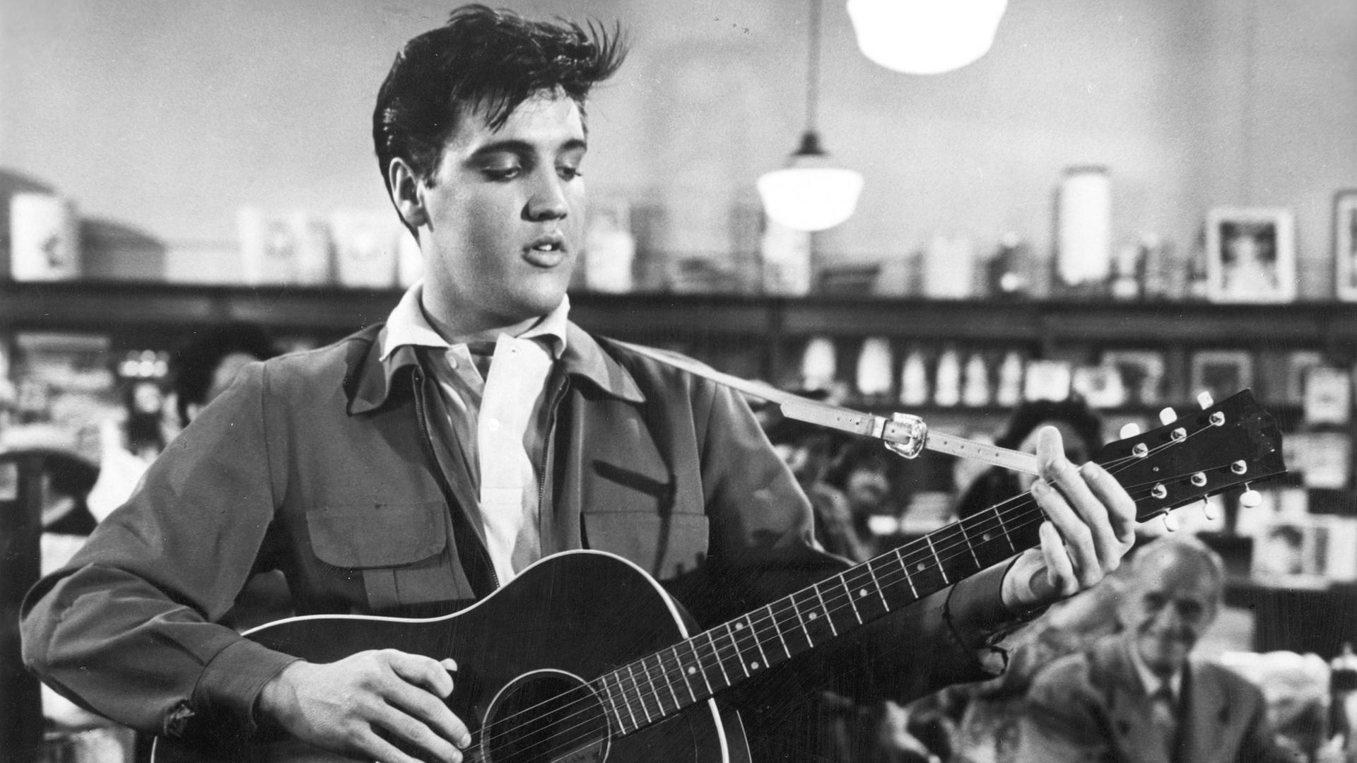 Schwarz-weiß-Foto von Elvis Presley mit Gitarre.