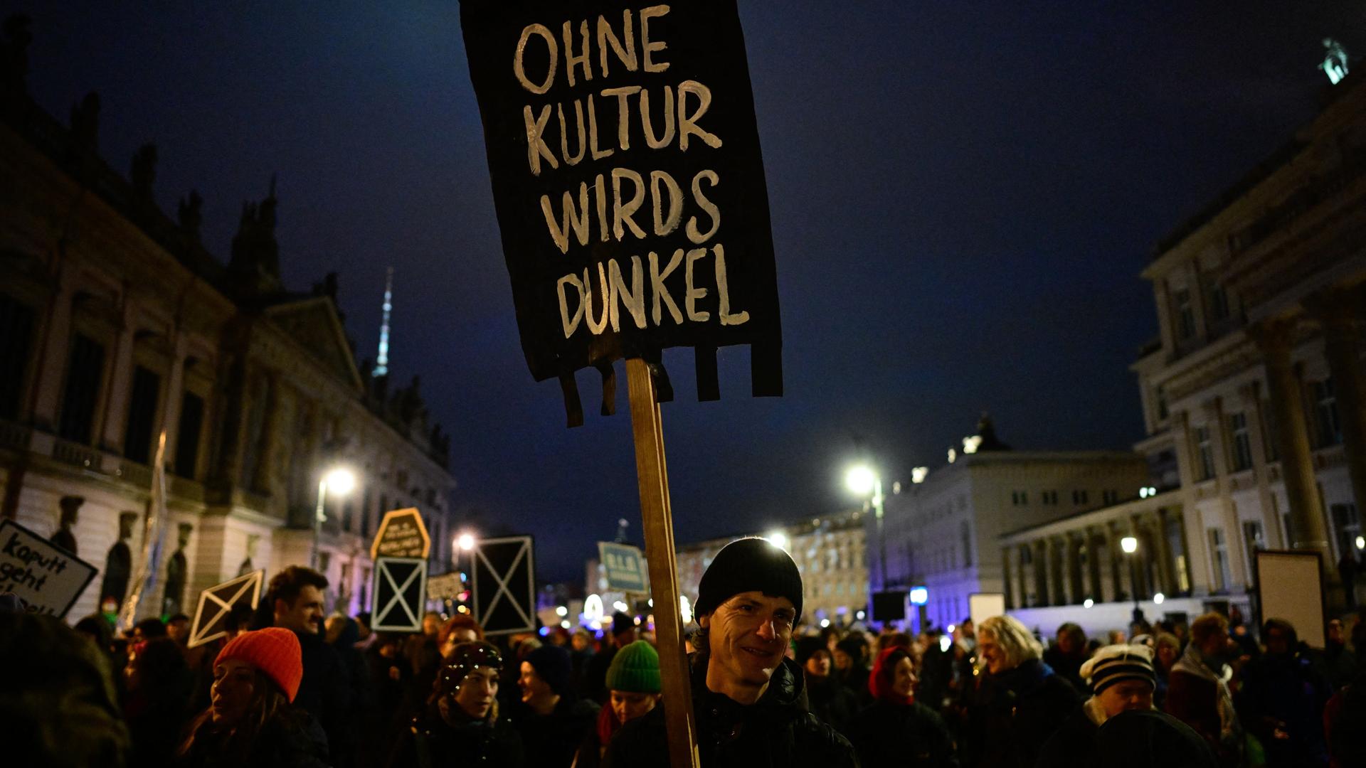 Ein Demonstrant hält ein schwarzes Schild hoch mit der Aufschrift "Ohne Kultur wirds dunkel"