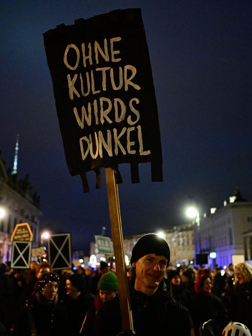 Ein Demonstrant hält ein schwarzes Schild hoch mit der Aufschrift "Ohne Kultur wirds dunkel"