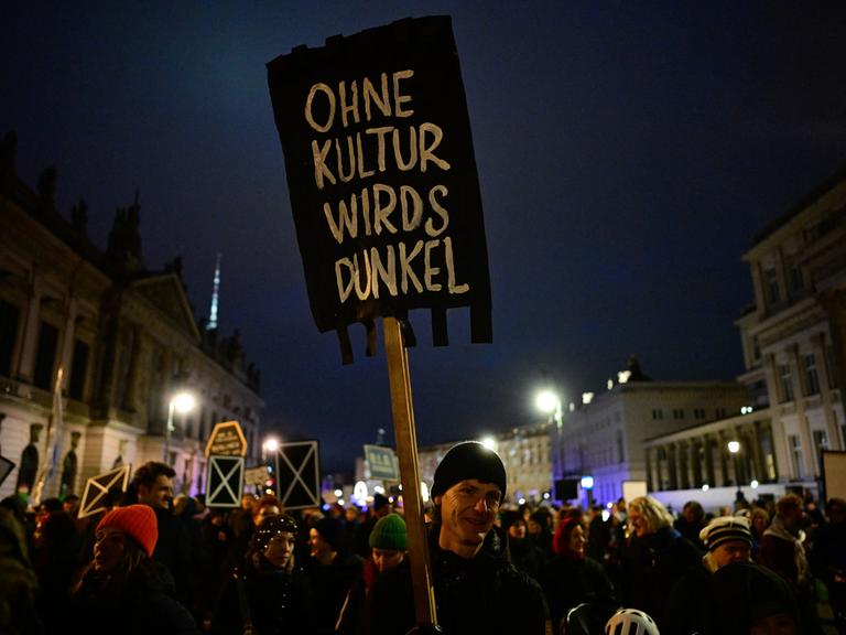 Ein Demonstrant hält ein schwarzes Schild hoch mit der Aufschrift "Ohne Kultur wirds dunkel"