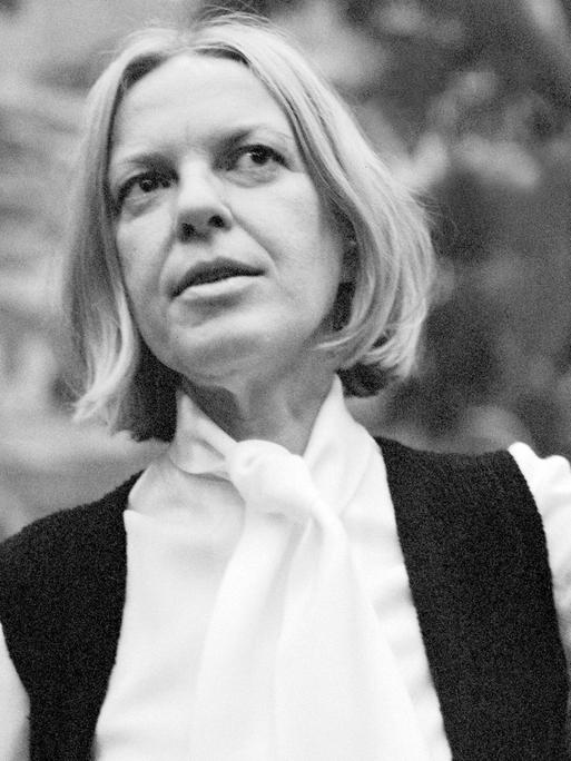 Ingeborg Bachmann steht in einem Garten und gestikuliert mit ihrer linken Hand in der Luft. Die Mittvierzigerin trägt auf dem Schwarz-Weiß-Bild eine helle Bluse und eine dunkle Weste darüber, ihre schulterlangen Haare sind gescheitelt.