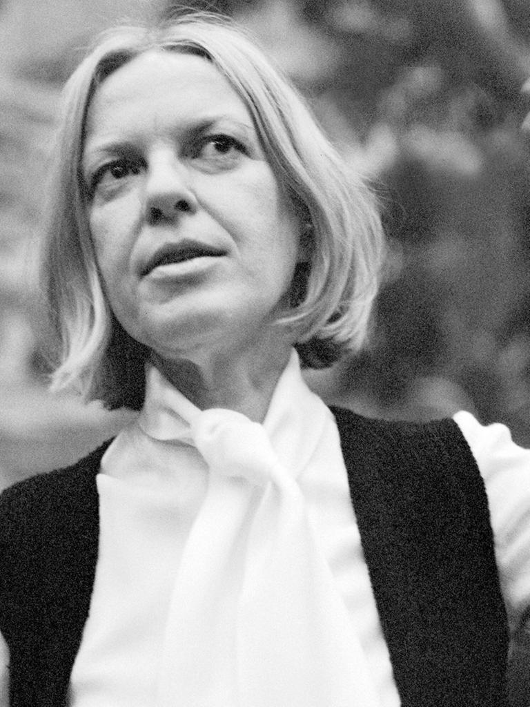 Ingeborg Bachmann steht in einem Garten und gestikuliert mit ihrer linken Hand in der Luft. Die Mittvierzigerin trägt auf dem Schwarz-Weiß-Bild eine helle Bluse und eine dunkle Weste darüber, ihre schulterlangen Haare sind gescheitelt.